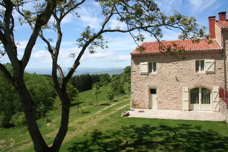 Maison en pierre sous tuiles rouges avec vue panoramique sur vallée boisée