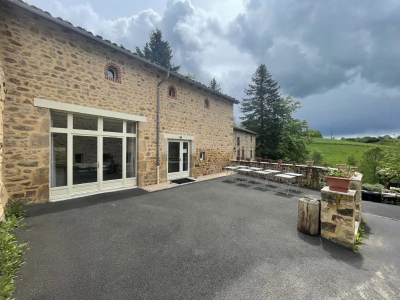 Bâtisse en pierre avec grandes baies vitrées et terrasse asphaltée