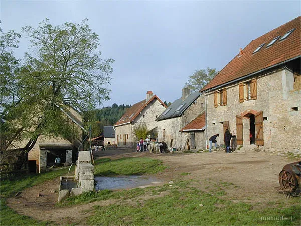 Cour de ferme en pierre avec puits et groupe d'enfants en activité