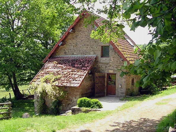 Grange en pierre avec toit en tuiles rouges et porte en bois, entourée de verdure