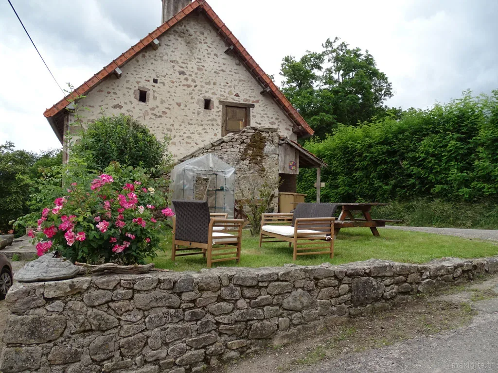 Façade en pierre avec roses trémières, transats en bois et muret rustique