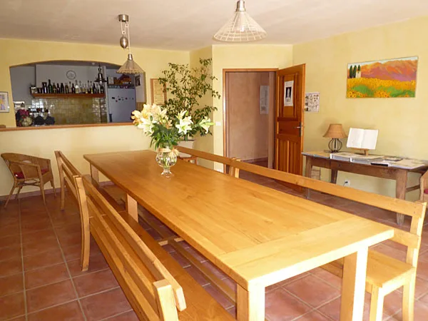 Salle à manger avec longue table en bois, bar et tableau coloré au mur
