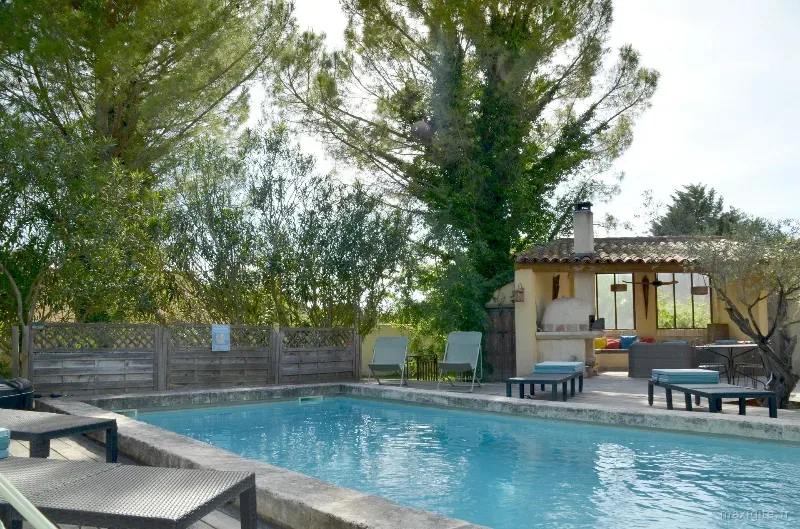 Piscine extérieure bordée de transats face à un pool house couvert avec coin salon ombragé
