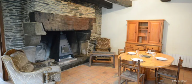 Séjour rustique avec immense cheminée en pierre, poêle, fauteuils et table à manger en bois clair