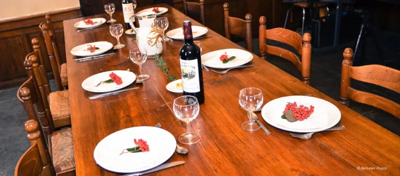 Longue table en bois dressée pour de nombreux convives avec assiettes, verres et chaises paillées