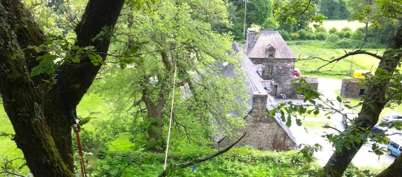 Vue lointaine des bâtisses en pierre nichées dans la végétation, aperçues à travers les arbres