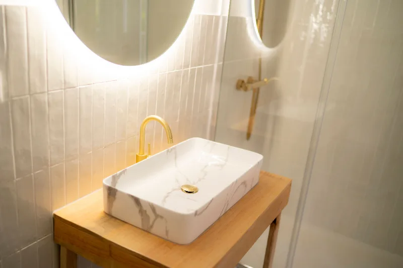 Salle d'eau moderne avec vasque en marbre, robinetterie dorée, miroir rétroéclairé et douche à l'italienne