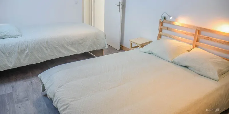 Chambre sobre avec un lit double à tête en bois et un lit simple, parquet clair et liseuse murale