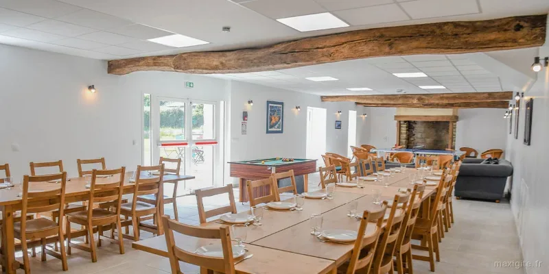 Grande salle de réception aux poutres apparentes, longues tables dressées, billard et cheminée en pierre
