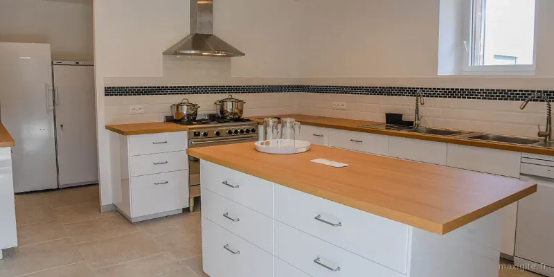 Grande cuisine fonctionnelle avec îlot central, plans de travail bois, piano de cuisson et réfrigérateur