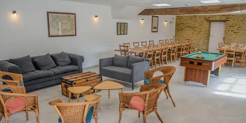 Vaste salle à vivre avec canapés, billard et longues tables en bois pour accueillir de nombreux convives