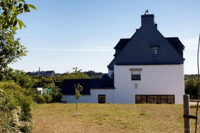 Grande maison blanche au toit d'ardoise pentu entouree d'un vaste terrain herbe ensoleille