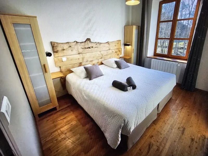 Chambre avec lit double, tete de lit en bois brut, parquet et fenetre sur la foret