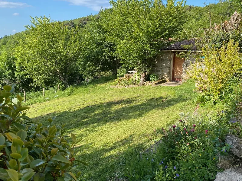 Petite dependance en pierre dans un jardin verdoyant arbore baigne de soleil