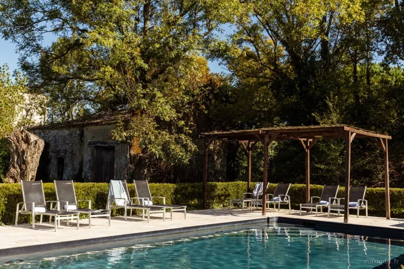 Piscine entouree de transats et pergola en bois, grands arbres offrant de l'ombre