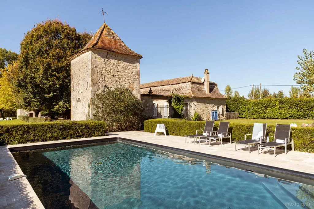 Gîte de groupe Chartreuse des Moulins à Montazeau — Chartreuse en pierre avec tour ancienne et piscine bordee de transats sous ciel bleu, capacité 15 personnes