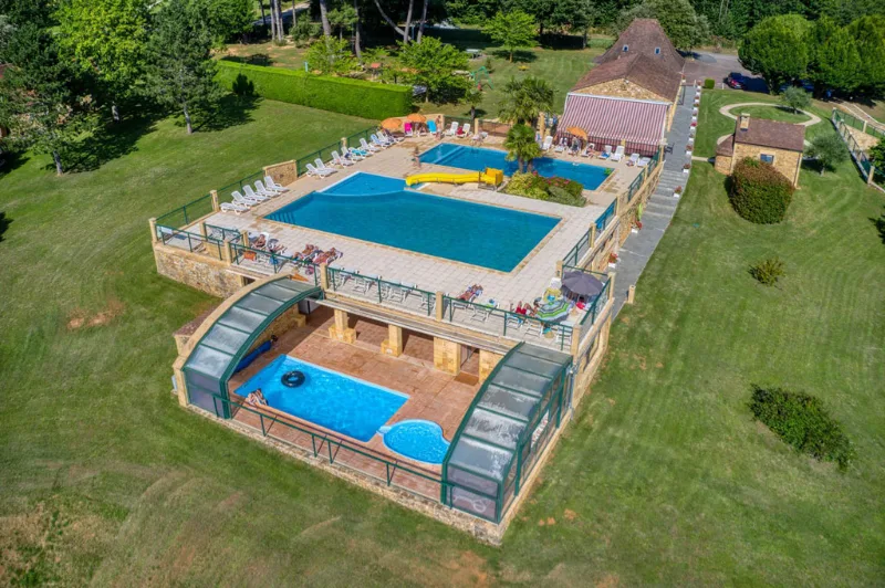 Grande piscine extérieure vue du ciel avec terrasse, transats et pelouse verdoyante alentour