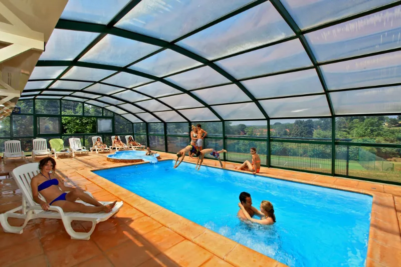 Piscine couverte sous véranda vitrée avec transats et baigneurs profitant de la lumière naturelle