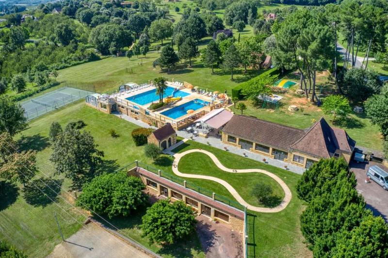 Vue aérienne du domaine avec gîtes en pierre, vaste pelouse, piscine et jardin paysager