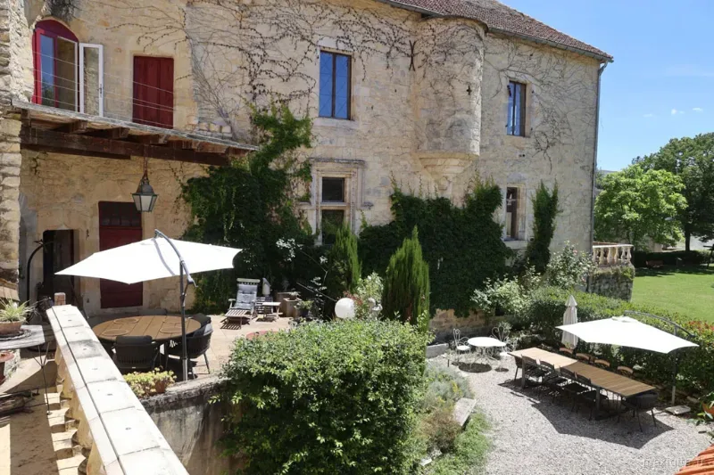Façade en pierre du château avec terrasse ombragée, parasols et jardin verdoyant ensoleillé
