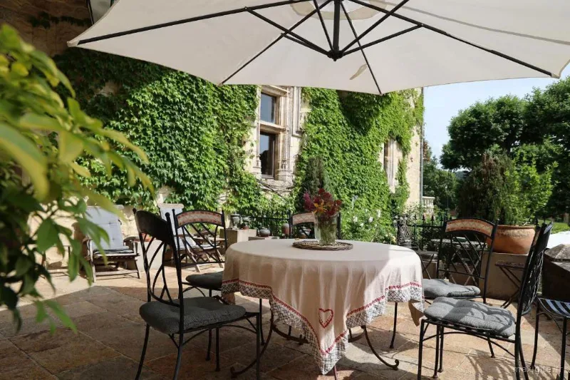 Terrasse extérieure avec table dressée sous parasol et mur tapissé de vigne vierge