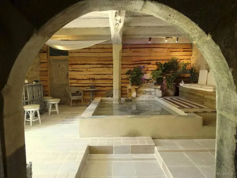 Espace bien-être voûté en pierre avec bassin, plantes vertes et coin détente sous poutres