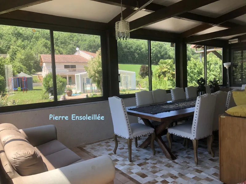 Véranda lumineuse avec grande table à manger, chaises capitonnées et baies vitrées sur la vallée
