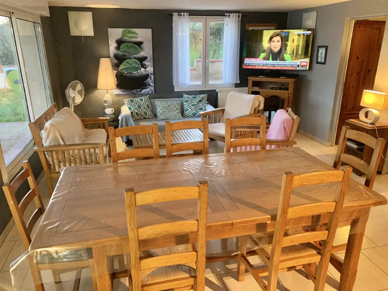 Salon convivial avec table en bois, fauteuils, canapé et écran télévision dans pièce de vie