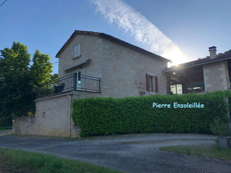 Façade en pierre avec balcon en fer forgé, haie taillée et cour gravillonnée ensoleillée