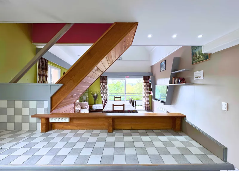 Espace de vie en mezzanine avec escalier bois, carrelage damier et vue jardin