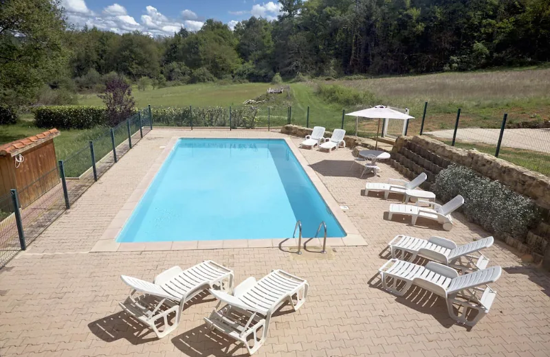 Piscine extérieure sécurisée entourée de transats et de terrasse dallée face aux prairies