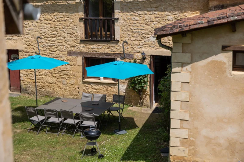 Cour intérieure en pierre avec tables, parasols bleus et plancha pour repas conviviaux en plein air