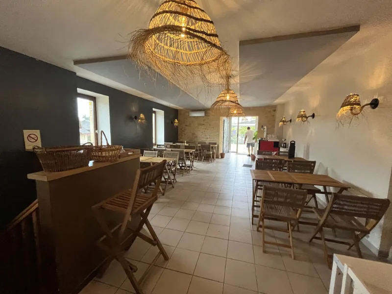 Salle à manger lumineuse aux suspensions en osier, tables en bois et accès vers la cour extérieure