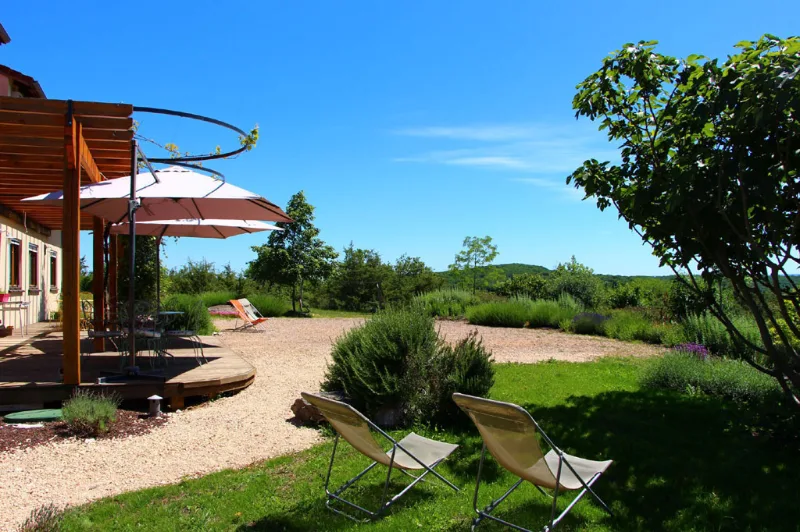 Terrasse en bois avec pergola, parasol et transats face au jardin et campagne vallonnée