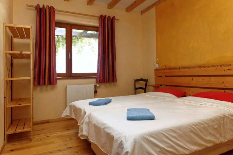 Chambre lumineuse aux murs ocre avec grand lit, étagère en bois et fenêtre rideaux rayés