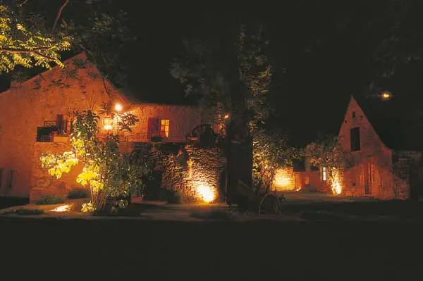 Façades en pierre du hameau illuminées à la nuit tombée, éclairage chaleureux et végétation mise en valeur