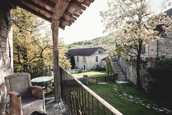 Terrasse couverte avec fauteuil en osier dominant la cour engazonnée et les bâtisses en pierre