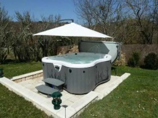 Spa de nage extérieur avec parasol sur terrasse pavée bordée de jardin et haies arborées