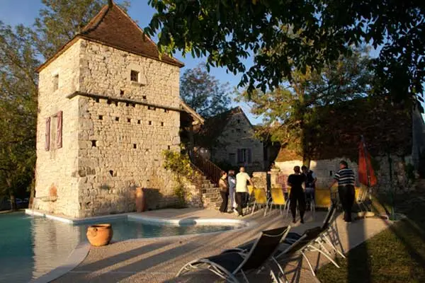 Piscine et plage avec transats devant le pigeonnier en pierre, groupe d'invités au coucher du soleil