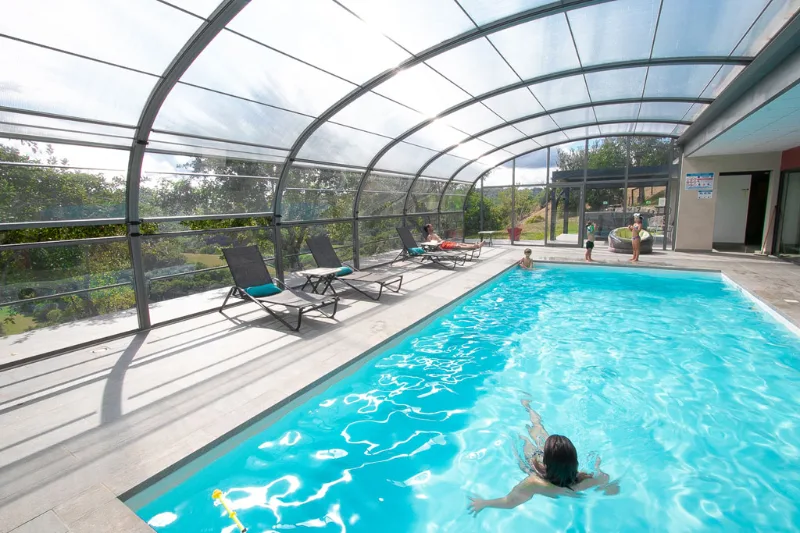 Piscine intérieure couverte d'un abri vitré avec transats, baigneurs profitant de l'espace lumineux