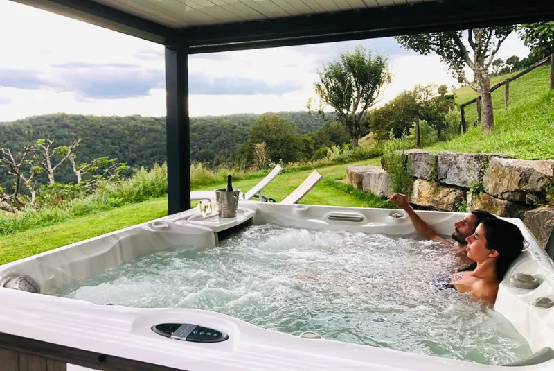 Spa extérieur où se détend une personne avec vue panoramique sur les collines verdoyantes