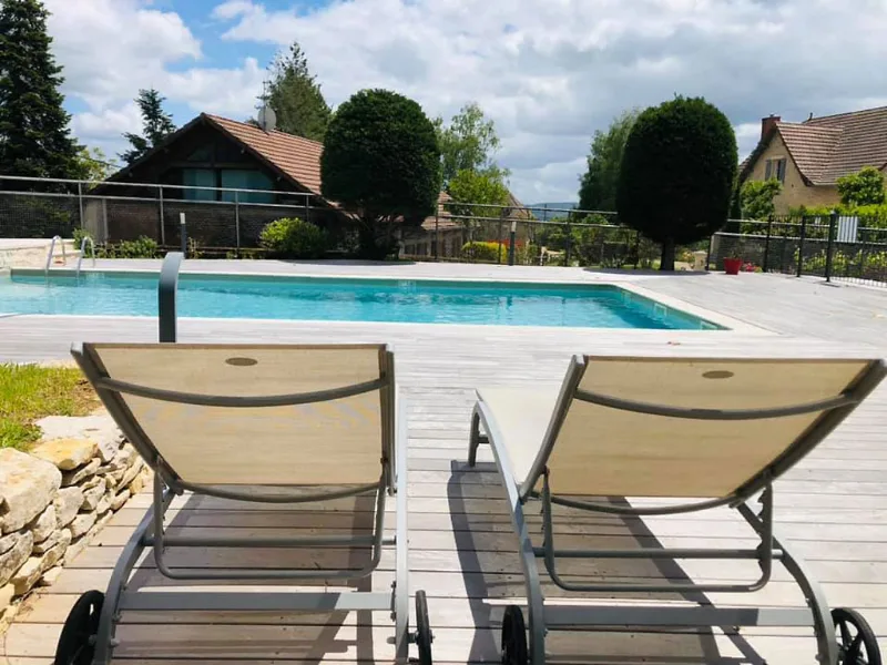Bains de soleil sur terrasse en bois au bord de la piscine, maisons et campagne en arrière-plan