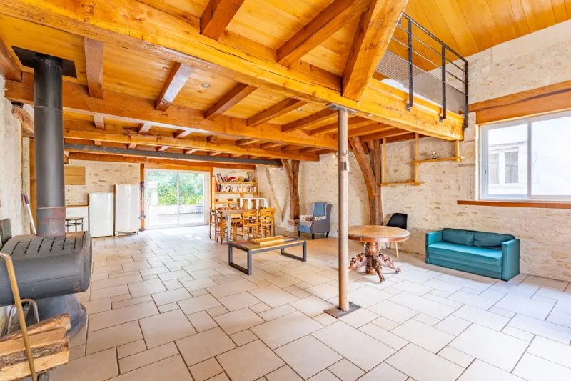 Vaste séjour aux murs en pierre avec poêle à bois, coin repas et mezzanine sous charpente apparente