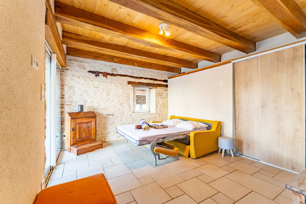 Chambre aux murs en pierre avec canapé-lit jaune, baie vitrée lumineuse et placard coulissant bois