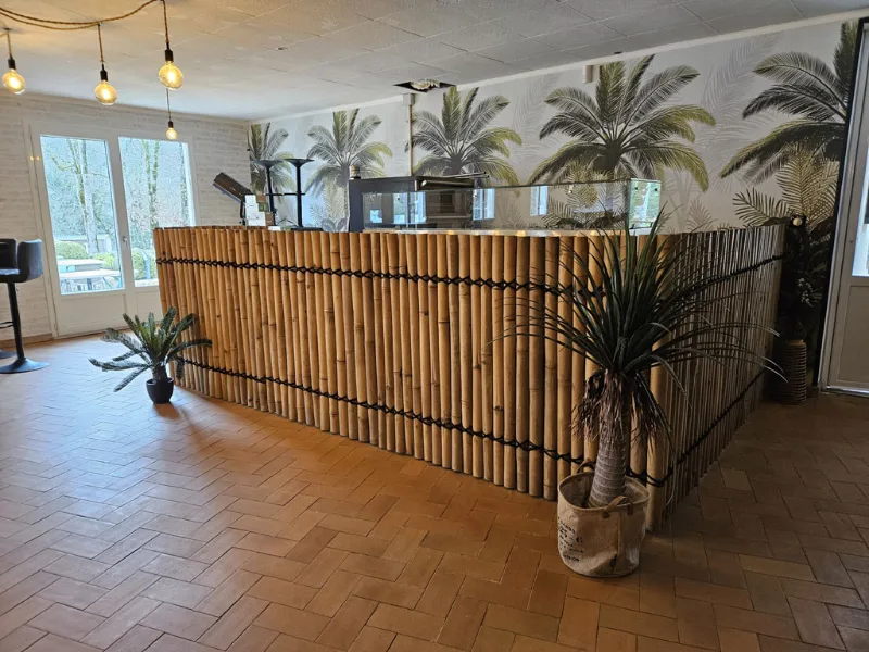 Bar habillé de bambou devant une fresque de palmiers, plantes en pot et sol en tomettes