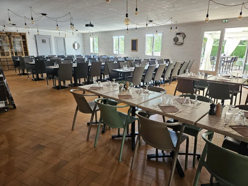 Vaste salle de réception avec nombreuses tables dressées, suspensions design et baies sur la terrasse