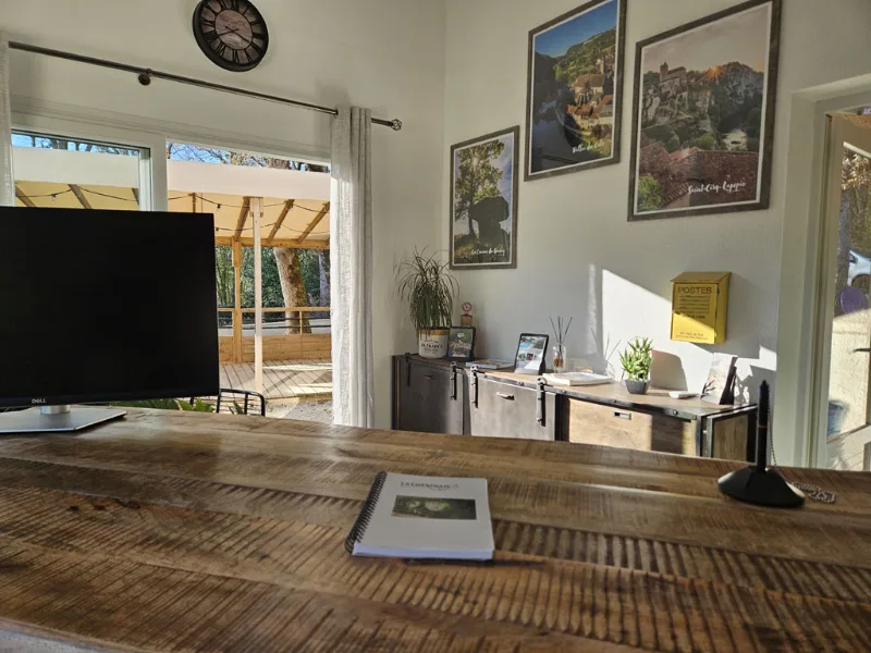 Comptoir d'accueil en bois avec écran et affiches régionales, terrasse visible par la baie vitrée