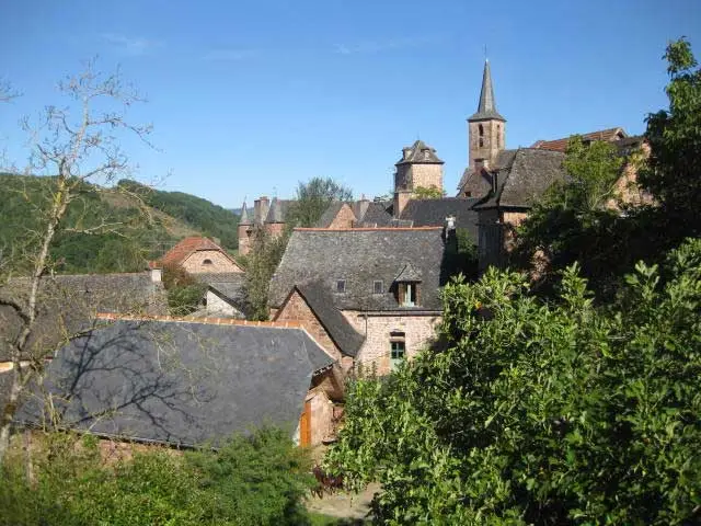 Vue sur les toits en lauzes et le clocher du village ancien entouré de verdure et collines