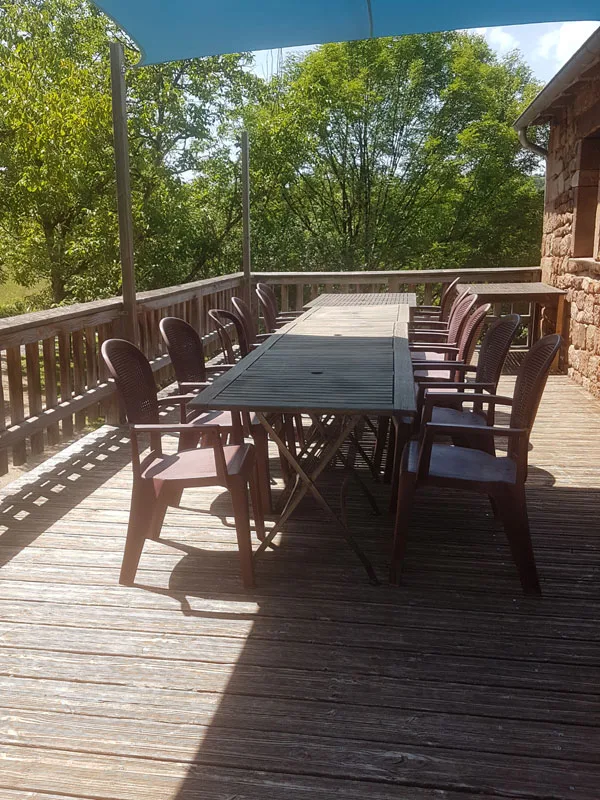 Terrasse en bois ombragée avec grande table et fauteuils accueillant une dizaine de convives