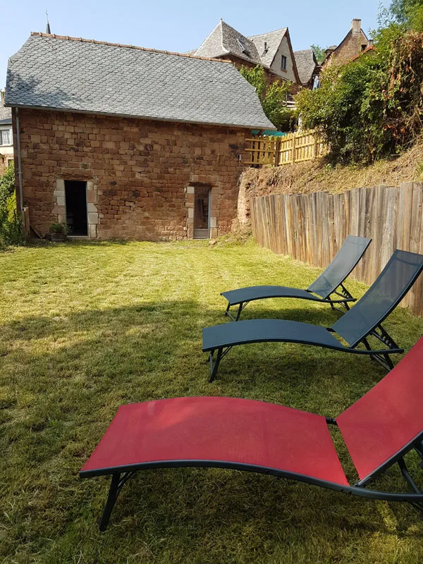 Jardin engazonné avec transats colorés devant une dépendance en pierre rouge ensoleillée